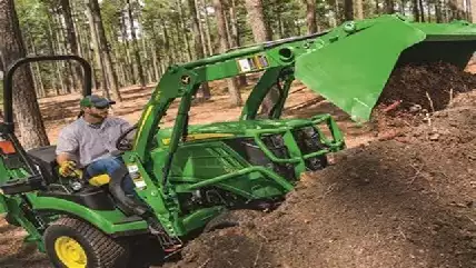 Picture of a landscape contractor using a John Deere tractor to move soil he is clearing